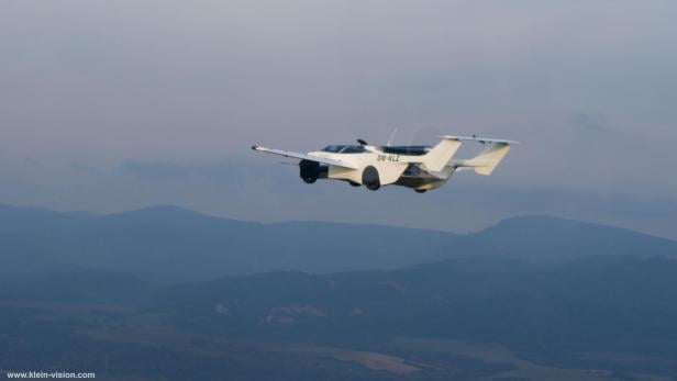 Das AirCar fliegt wie ein Kleinflugzeug und fährt wie ein Sportwagen. Das AirCar in der Luft, im Hintergrund eine Bergkette